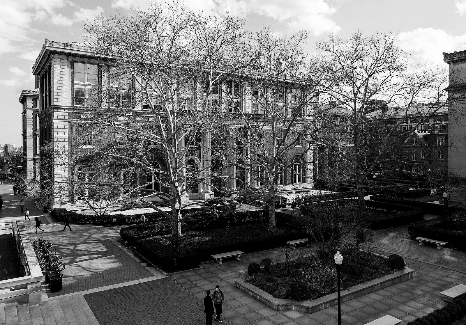 Black and white photo of Avery Hall at Columbia University, a historic building with classical architecture, where Norma Sklarek, a pioneering African American architect, once studied. The image captures the hall's grandeur, framed by leafless trees and a serene courtyard, with students and faculty members walking by, illustrating the vibrant academic life within.